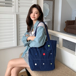 Detail of dark blue corduroy tote bag with colorful buttons in a bright indoor setting