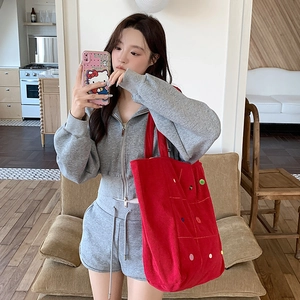 Detailed close-up of red corduroy tote bag with colorful buttons on a casual outfit