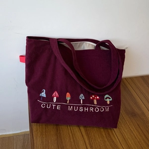 Detail of burgundy corduroy tote bag featuring six colorful cute mushroom embroideries