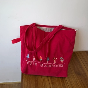Close-up of red corduroy tote bag featuring cute mushroom embroidery and zip closure