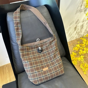 Macro detail of brown plaid woolen crossbody bag with drawstring closure on a leather chair