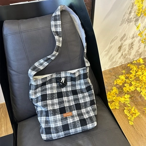 Close-up of black and white plaid wool tote bag with toggle closure on leather sofa