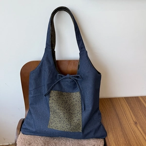 Detail of blue denim tote bag with green leopard print patch and a decorative ribbon bow