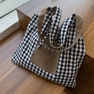 Detail view of a black and white checkered tote bag with brown suede pocket on wooden steps