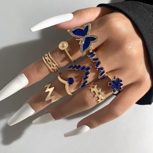 Ensemble de bagues dorées avec papillon, étoiles et strass bleus portés par un modèle
