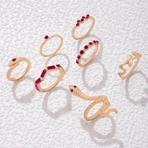 Ensemble de sept bagues dorées avec pierres rouges et motifs de serpents détaillés sur fond blanc