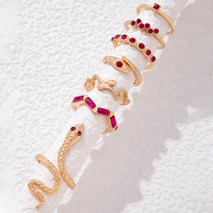 Détail de bagues serpent dorées avec cristaux rouges sur un support d'exposition blanc
