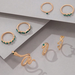 Détail d'un lot de 7 bagues serpent dorées serties de pierres vertes sur fond gris