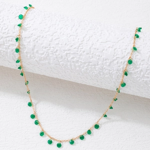 Detail of bohemian gold chain with small green translucent stones on textured white base