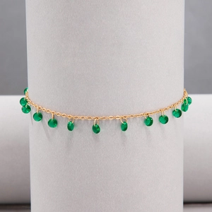Close-up of gold chain with faceted green stone pendants on a grey display stand