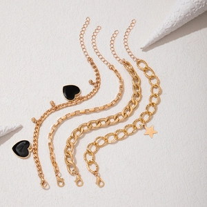 Detail of four gold bracelets set with black heart charms and star pendant on coral
