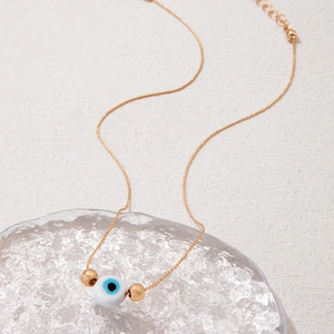 Detail of gold evil eye necklace with blue bead pendant on a glass tray background