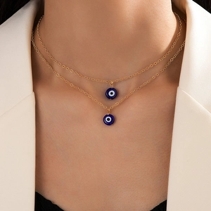 Gold double-layered necklace with blue evil eye pendants worn with a beige blazer