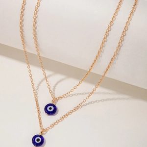 Close-up of golden layered necklace with dual blue Evil Eye charms and fine link chain