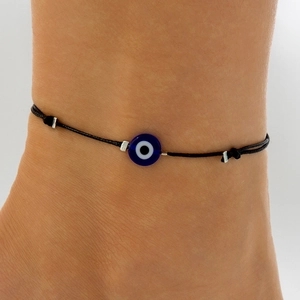 Detail of hand-woven black string anklet featuring a classic blue evil eye charm bead