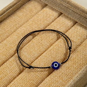 Macro shot of an adjustable black cord bracelet with a blue Evil Eye bead on a tray