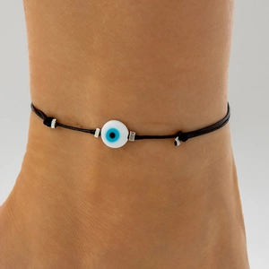 Detailed view of a black cord ankle bracelet with blue evil eye bead and silver charms