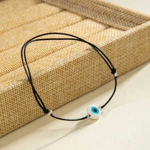 Detail of hand-woven black string bracelet with blue and white evil eye bead accent