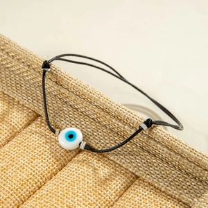 Detailed macro view of an Evil Eye bead on a black woven cord bracelet on rustic straw
