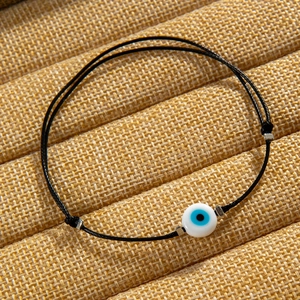 Close-up of a blue evil eye bead on a black woven cord necklace against a textured backdrop