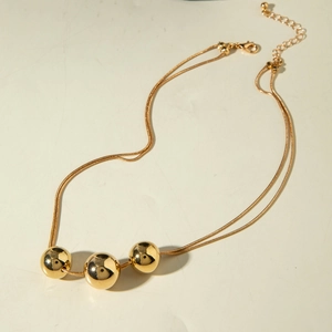 Close-up of a double-layer gold snake chain necklace with three polished metal beads