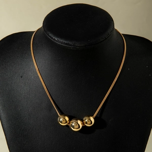 Detailed view of gold snake chain necklace featuring three polished spherical beads
