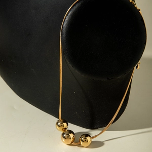 Detail of three polished gold beads on a delicate chain necklace over black velvet