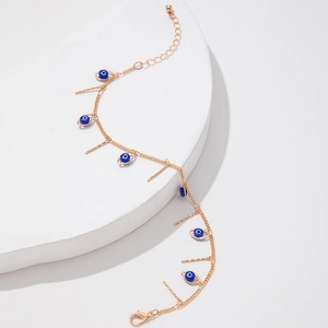Detail of gold evil eye bracelet with blue charms and vertical bars on a white stand