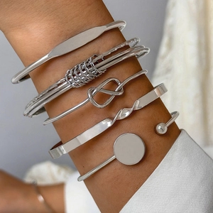 Close-up of stacked silver minimalist geometric bangles featuring knots and polished textures
