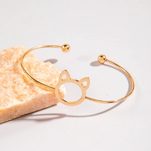 Bracelet doré à pendentif chat évidé posé sur un support en pierre naturelle