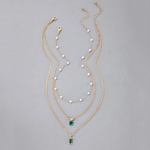 Détail d'un collier doré multicouche avec perles et pendentifs en cristal vert émeraude