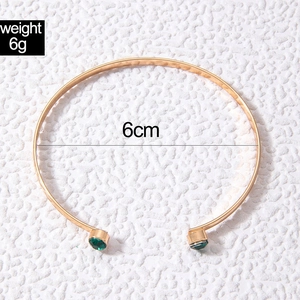 Macro shot of gold cuff bracelet with 6cm inner diameter and green stone accents