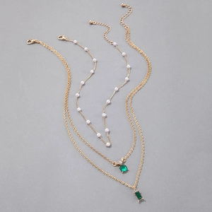Détail d'un collier triple couche doré avec perles et pierres précieuses vert émeraude