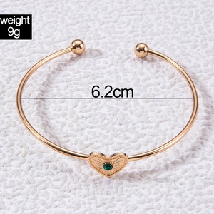 Macro detail of gold-tone open cuff bracelet with green gemstone heart and weight info