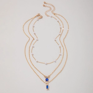 Détail d'un collier triple couche doré avec perles et pendentifs pierres bleu profond
