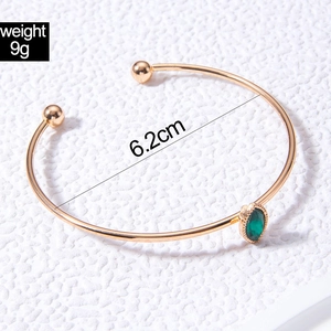 Detail showing gold C-shaped cuff bracelet with green stone inlay and 6.2cm diameter
