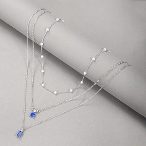 Détail macro d'un collier argenté multicouche avec pendentifs émeraude et perles