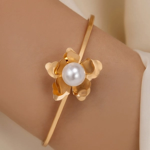 Close-up of golden petal open cuff bracelet with a central white pearl on a woman's wrist