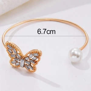 Close-up of gold open bracelet with butterfly rhinestone and pearl detail, 6.7cm diameter
