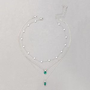 Détail d'un collier triple couche argenté avec pierres vert émeraude et perles