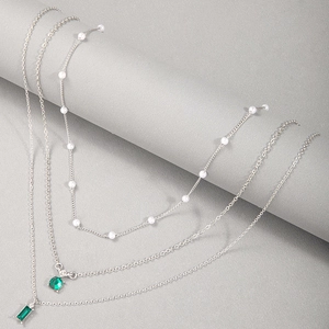 Détail de colliers superposés argentés avec pierres vert émeraude et perles blanches