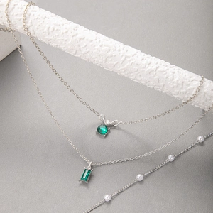 Détail du collier argenté multicouche avec des pierres vert émeraude et des perles blanches