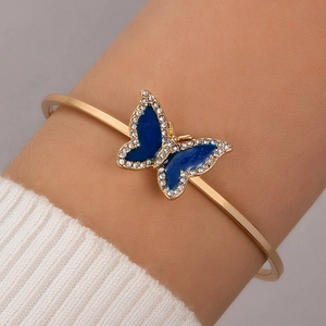 Close-up of gold open bracelet featuring a blue butterfly charm with crystals on wrist