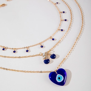 Détail d'un collier doré à plusieurs rangs avec perles bleues, cerise et cœur mauvais œil