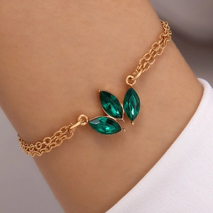 Detail view of a gold double-layer bracelet with leaf-shaped green gemstone settings