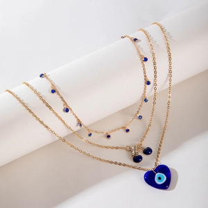 Détail d'un collier doré multicouche avec pendentif coeur bleu et charms cerise