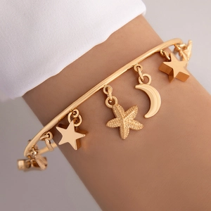 Detailed close-up of a gold open bangle featuring star, moon, and matte starfish charms