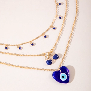 Détail du collier doré multicouche avec pierres bleues, pendentif cerise et cœur œil bleu