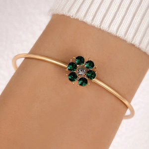 Detail of gold floral bangle with green petals and center crystal on a female wrist