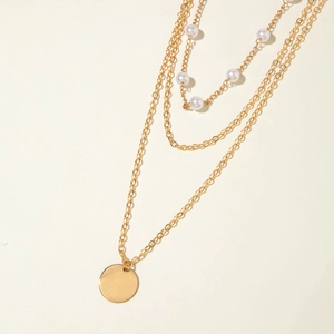 Détail d'un collier doré multicouche avec cinq perles et un pendentif rond en métal
